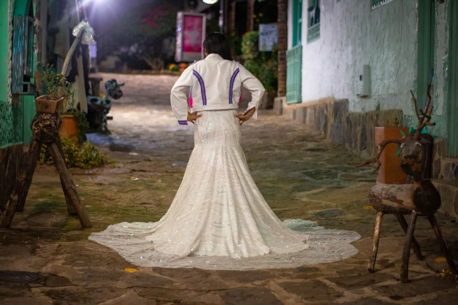 Espalda de una chaqueta blanca con detalles rosa y azul sobre vestido blanco bordado